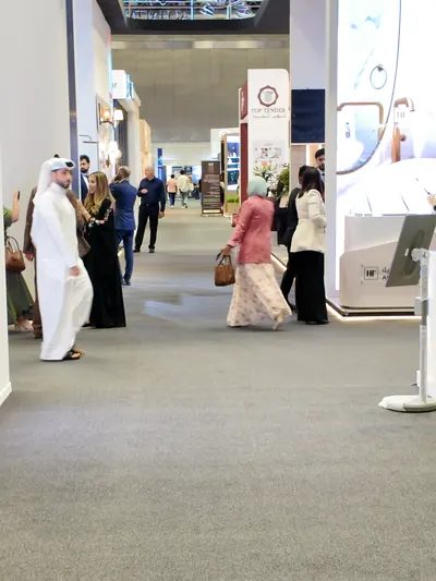 Visitors in abayas and thobes stroll between brightly lit exhibition stands.