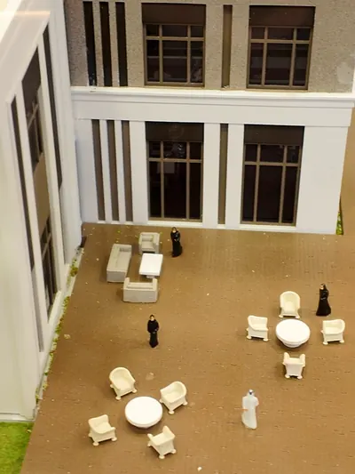 An architectural scale model of a villa courtyard, with miniature furniture and figures.